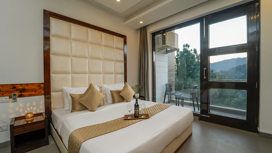 The premium room of DLS Whispering Winds with a bed, bed side tables, and a glass door leading to the balcony overlooking the mountain view